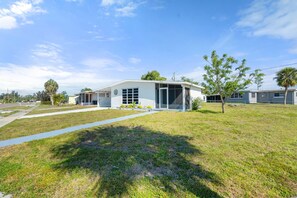 A single-story building with a large garage door, a small porch, and a lawn in front. - Nestled in North Port.  Updated 2 Bed / 1 Bath. (North Port)