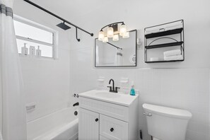 A modern bathroom with a white sink, black faucet, and a toilet. There is a window with a shower curtain and a towel rack above the sink. - Nestled in North Port.  Updated 2 Bed / 1 Bath. (North Port)