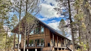 A modern log cabin with a large deck and multiple windows, surrounded by trees. - Buffalo Creek at Ponds Lodge Cabin 26 (Island Park)