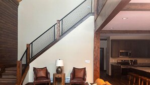 A spacious living area with a wooden staircase, leather sofas, a coffee table, and a kitchen in the background. - Buffalo Creek at Ponds Lodge Cabin 26 (Island Park)