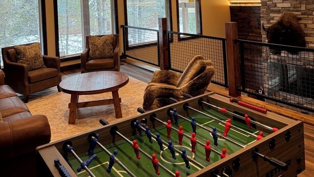 A cozy room with a foosball table, large windows, and a stone fireplace. - Buffalo Creek at Ponds Lodge Cabin 26 (Island Park)