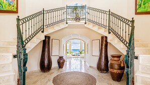 Un magnifique escalier offrant une vue sur la mer, menant à un vaste hall d’entrée agrémenté de grands vases et d’un tapis.