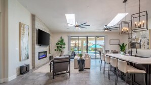 A modern kitchen with a central island, a dining area with bar stools, a flat-screen TV mounted on the wall, and a ceiling fan.
