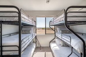Una stanza con tre letti a castello, una finestra vista deserto e una bocchetta di ventilazione al soffitto.