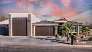 A modern two-story house with a garage, a driveway, and a landscaped front yard with palm trees.