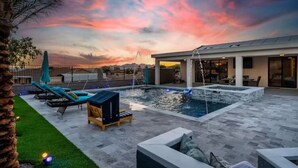 A modern outdoor pool area with lounge chairs, a hot tub, and a view of the sunset.