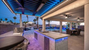 An outdoor kitchen area with a built-in grill, bar seating, and a pool in the background.