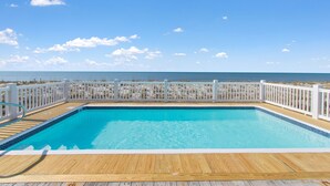 Piscina rectangular con muelle de madera y barandillas blancas, rodeada por una playa de arena y vista al océano.