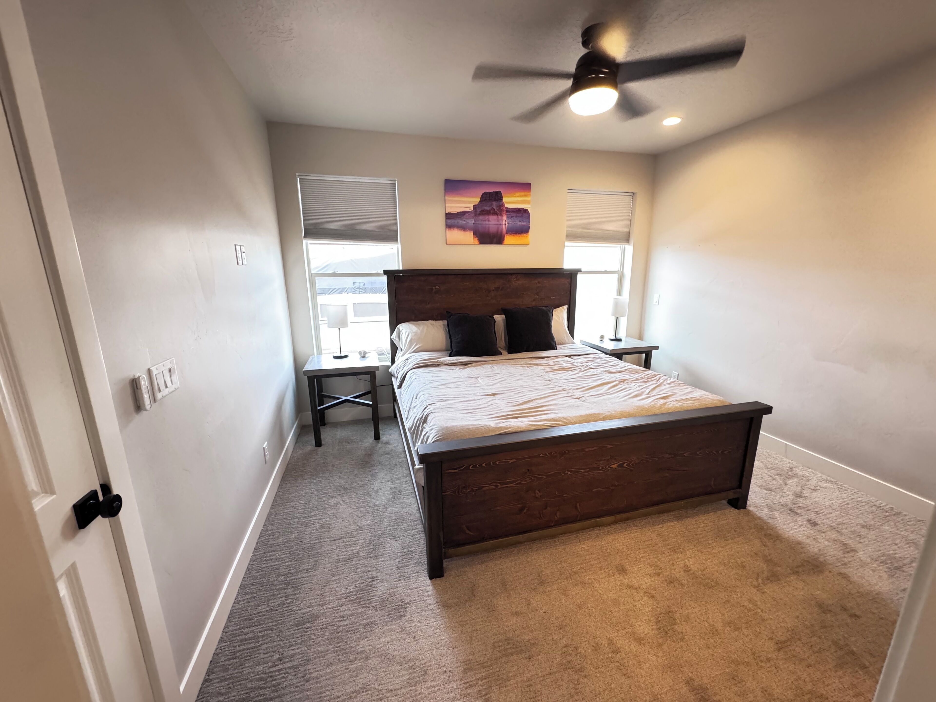 A bedroom with a bed, a desk, a ceiling fan, and a window with blinds.