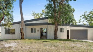Een modern gelijkvloershuis met garage, nummer 38, omringd door bomen en een gazon.