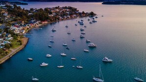 An aerial view of a coastal town with numerous boats anchored in the water, surrounded by residential buildings and a clear view of the coastline. - Sunlight Ridge House (Fishing Point)