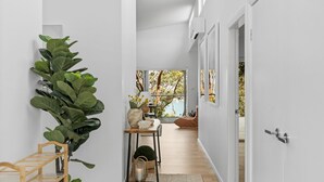 A modern hallway with a large potted plant, a wooden bench, and a table with decorative items. A view of a balcony with a wooden floor and a chair is visible through an open door. - Sunlight Ridge House (Fishing Point)