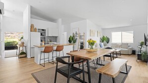 A modern kitchen with white cabinetry, a wooden island, and a dining area with a wooden table and chairs. - Sunlight Ridge House (Fishing Point)