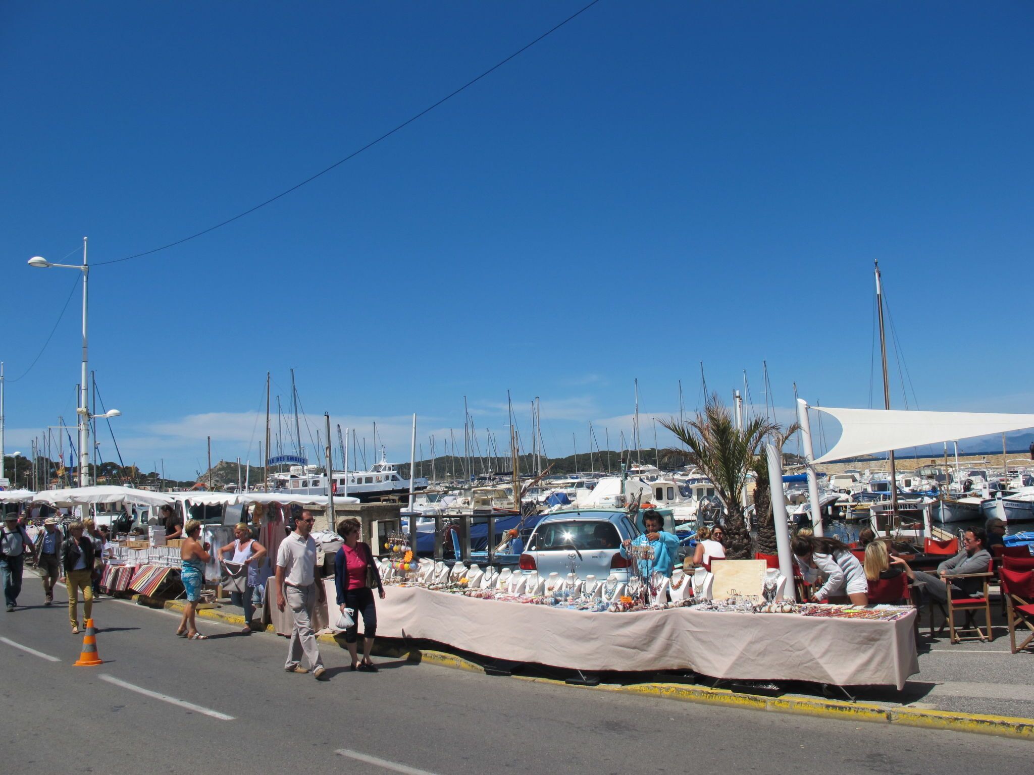 A marina with boats docked, a street with pedestrians, and a market stall with various items.