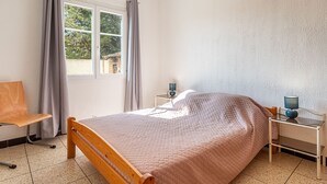 Un dormitorio con una cama de madera, un escritorio, una silla, una lámpara y una ventana con cortinas.