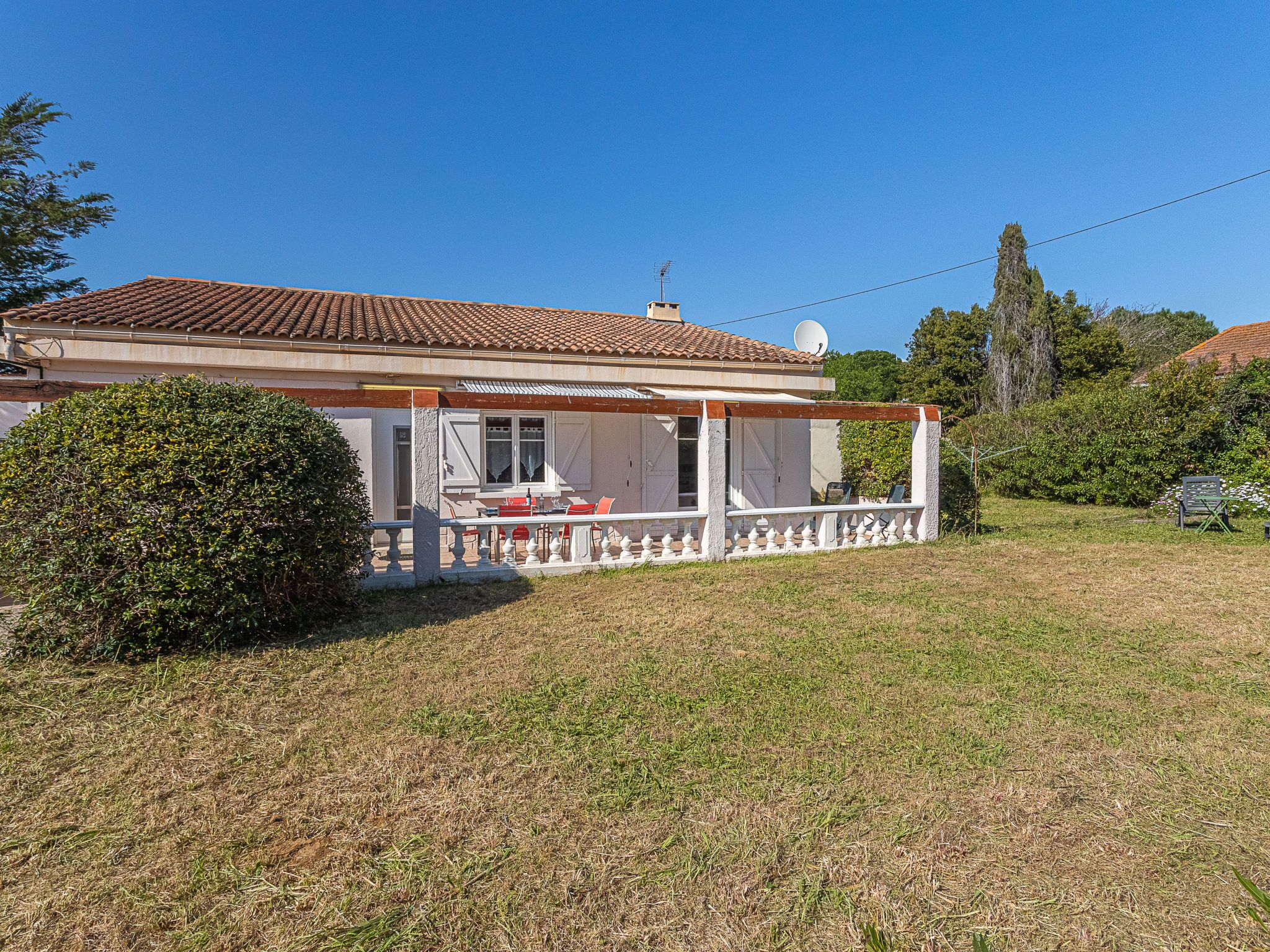 Une maison avec un toit recouvert de tuiles, une véranda couverte avec une balustrade blanche et une antenne parabolique sur le toit.