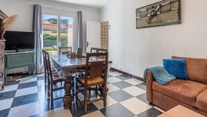 Un comedor con piso a cuadros, una mesa de madera, sillas, un televisor sobre un mueble bajo y un cuadro en la pared.