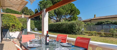An outdoor dining area with a table set for four, surrounded by red chairs, under a striped awning.