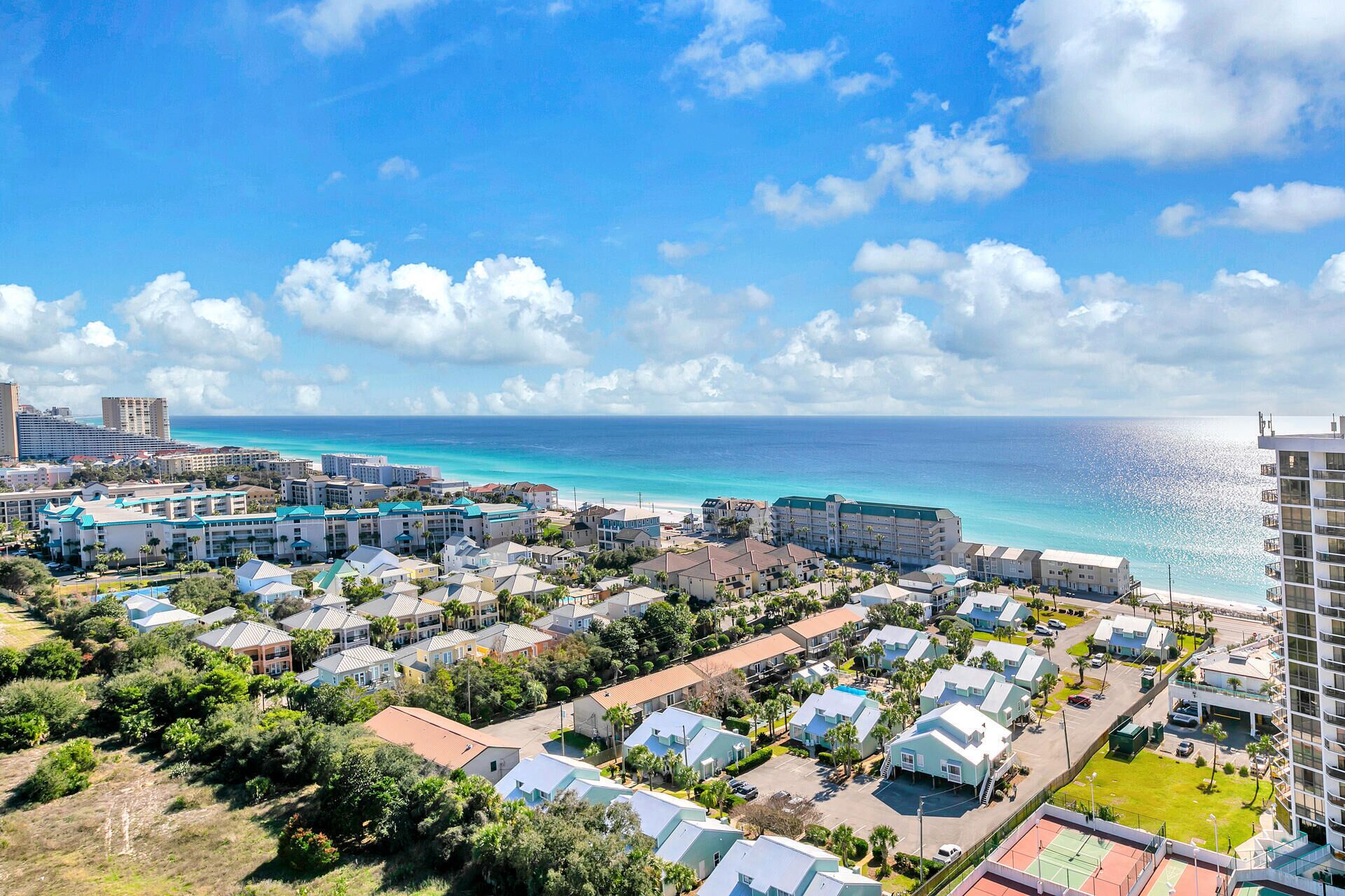 A coastal resort area with multiple buildings, including hotels and residential structures, with a view of the ocean and clear skies.