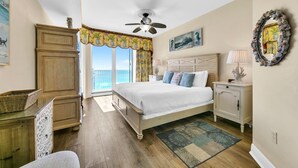 A bedroom with a large bed, a ceiling fan, a nightstand, a dresser, and a view of the outdoors.