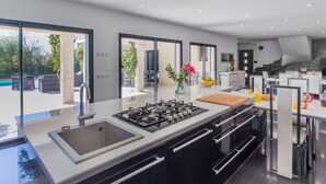 A modern kitchen with a gas stove, sink, and a large island. There is a dining area with a table and chairs visible through glass doors. - Vacation home Villa by Interhome (Saint Cyr sur mer Les Lecques)