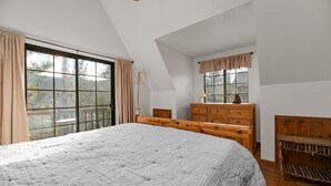A bedroom with a large bed, wooden dresser, and a window with curtains.