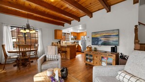 A spacious living area with wooden flooring, a dining table with chairs, a sofa, and a kitchen in the background.