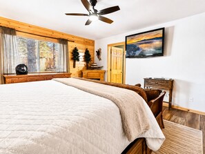 Une chambre avec un grand lit, un ventilateur de plafond, une télévision et une fenêtre avec des rideaux.