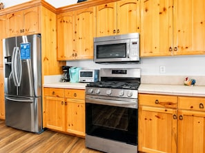 A kitchen with wooden cabinets, a stainless steel refrigerator, a microwave, a toaster, and a stove.