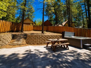 Un patio trasero con muro de piedra, escalones de madera, mesa de picnic y bañera de hidromasaje.