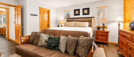 A bedroom with a bed, a wooden headboard, a ceiling fan, a nightstand with lamps, a dresser, and a wooden door.