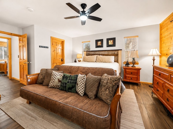 A bedroom with a bed, a wooden headboard, a ceiling fan, a nightstand with lamps, a dresser, and a wooden door.