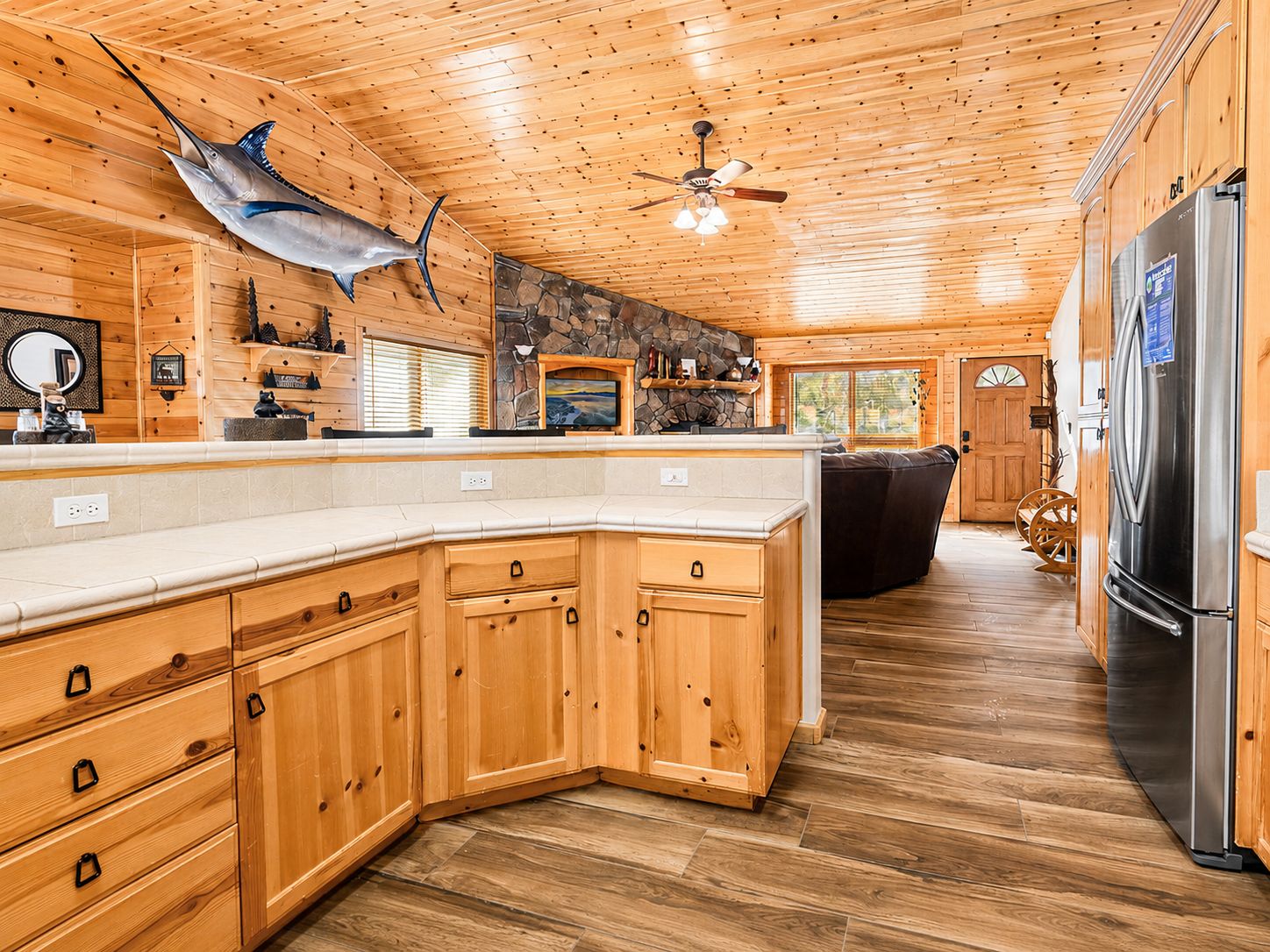A wooden interior with a stone fireplace, a ceiling fan, and a large refrigerator.