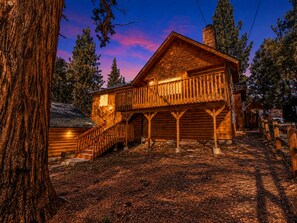 Une cabane en rondins dotée d’un balcon, entourée d’arbres et d’une clôture en bois.