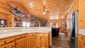 L’intérieur d’une cabane en bois comprend une grande cuisine, une cheminée en pierre et un ventilateur de plafond.