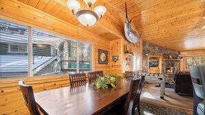 L’intérieur d’un chalet en bois comprend une table à manger, des chaises, un lustre, une cheminée en pierre et un coin cuisine.