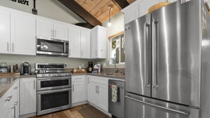 A modern kitchen with stainless steel appliances, white cabinetry, and a wooden floor.