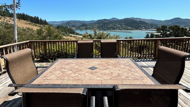 A deck with a table and chairs overlooking a lake and mountains. - Fantastic River & Ocean Views! Family Friendly Home, Sleeps 8 (Gold Beach)