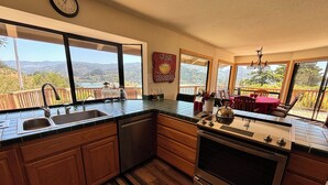 A kitchen with a view of the mountains, wooden cabinets, a stainless steel stove, and a sink. - Fantastic River & Ocean Views! Family Friendly Home, Sleeps 8 (Gold Beach)