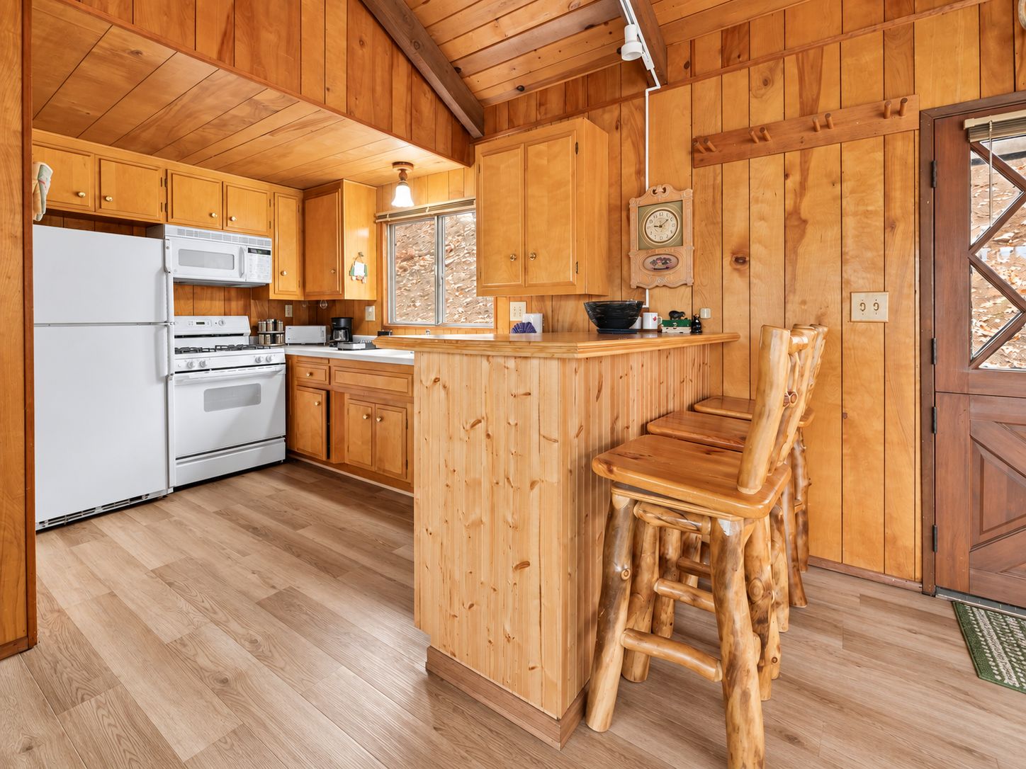 Una cocina con armarios de madera, un refrigerador blanco, una estufa y un taburete de bar de madera.