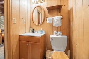 Une salle de bain en bois, avec un meuble-lavabo en bois, des toilettes, un miroir et un porte-serviettes.