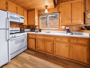 A kitchen with wooden cabinets, a white refrigerator, a stove, and a window with a view of trees.