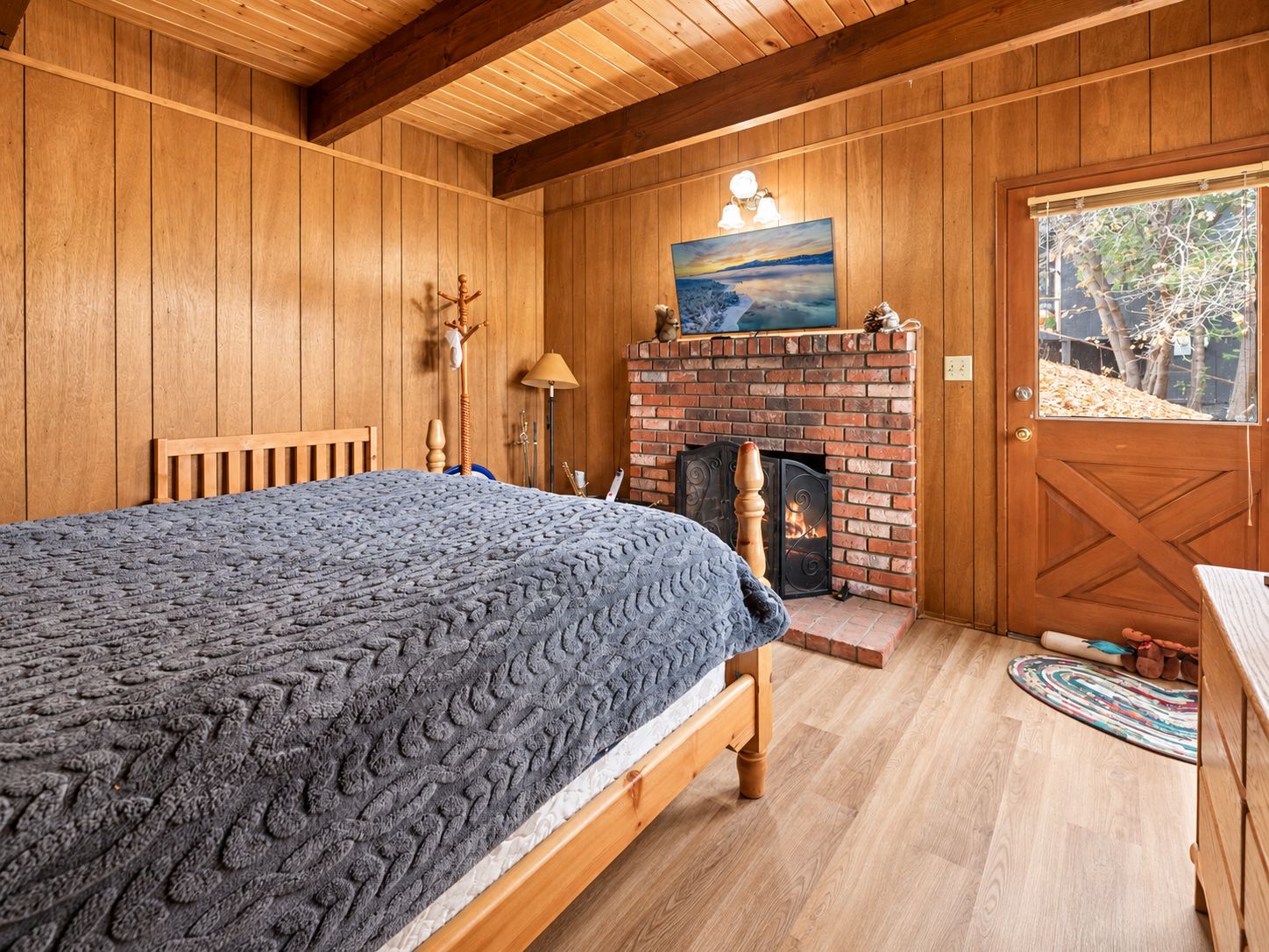 Una habitación acogedora con cama, chimenea, paredes de madera y una puerta que da al exterior.