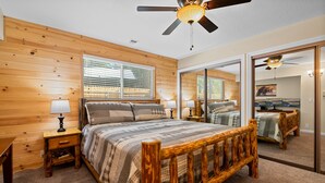 A bedroom with a wooden bed, bedside tables, a ceiling fan, and a large mirror.