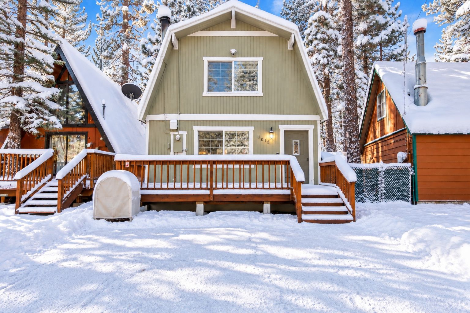 Une cabane en rondins à deux étages, dotée d’une terrasse en bois et d’une cheminée, entourée d’arbres couverts de neige.