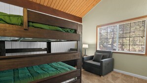 Ein Stockbett mit grüner Bettwäsche, ein grauer Sessel und ein Fenster mit Jalousien.