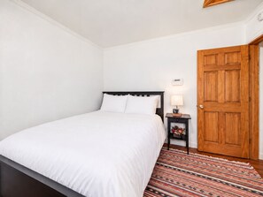 Een hotelkamer met een bed, een nachtkastje met een lamp, een houten deur en een kamerkleed met dessin.