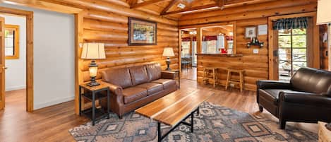 A log cabin interior with a wooden ceiling, a leather sofa, a wooden coffee table, and a patterned rug.