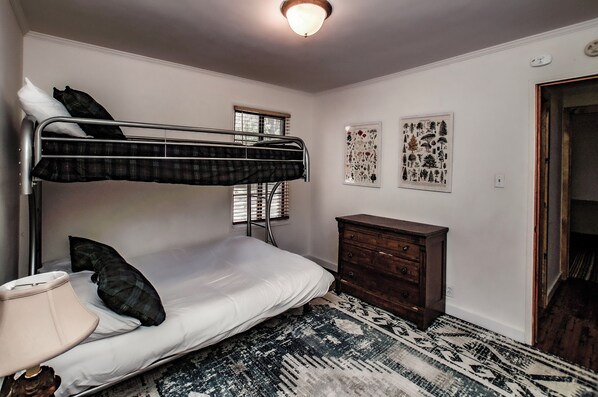 Een slaapkamer met een stapelbed, een houten dressoir, een kamerbreed tapijt met patroon en twee decoratieve wandobjecten.