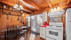 A wooden interior with a dining table, chairs, a stove, and a refrigerator.